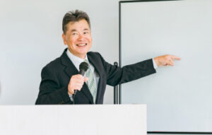 マイクを持って講義をするスーツ姿の男性